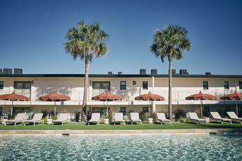 A hotel with a pool and palm trees in front.